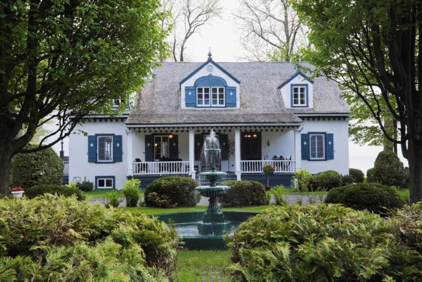A beautiful older home with blue shutters and a water fountain in front