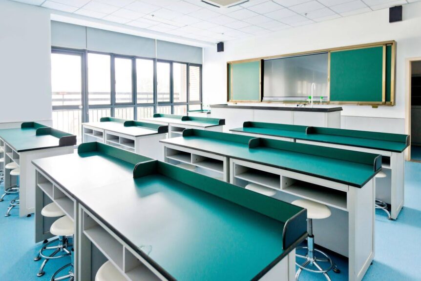 A classroom full of color with turquoise desks, white chairs, and a blackboard with windows letting in light