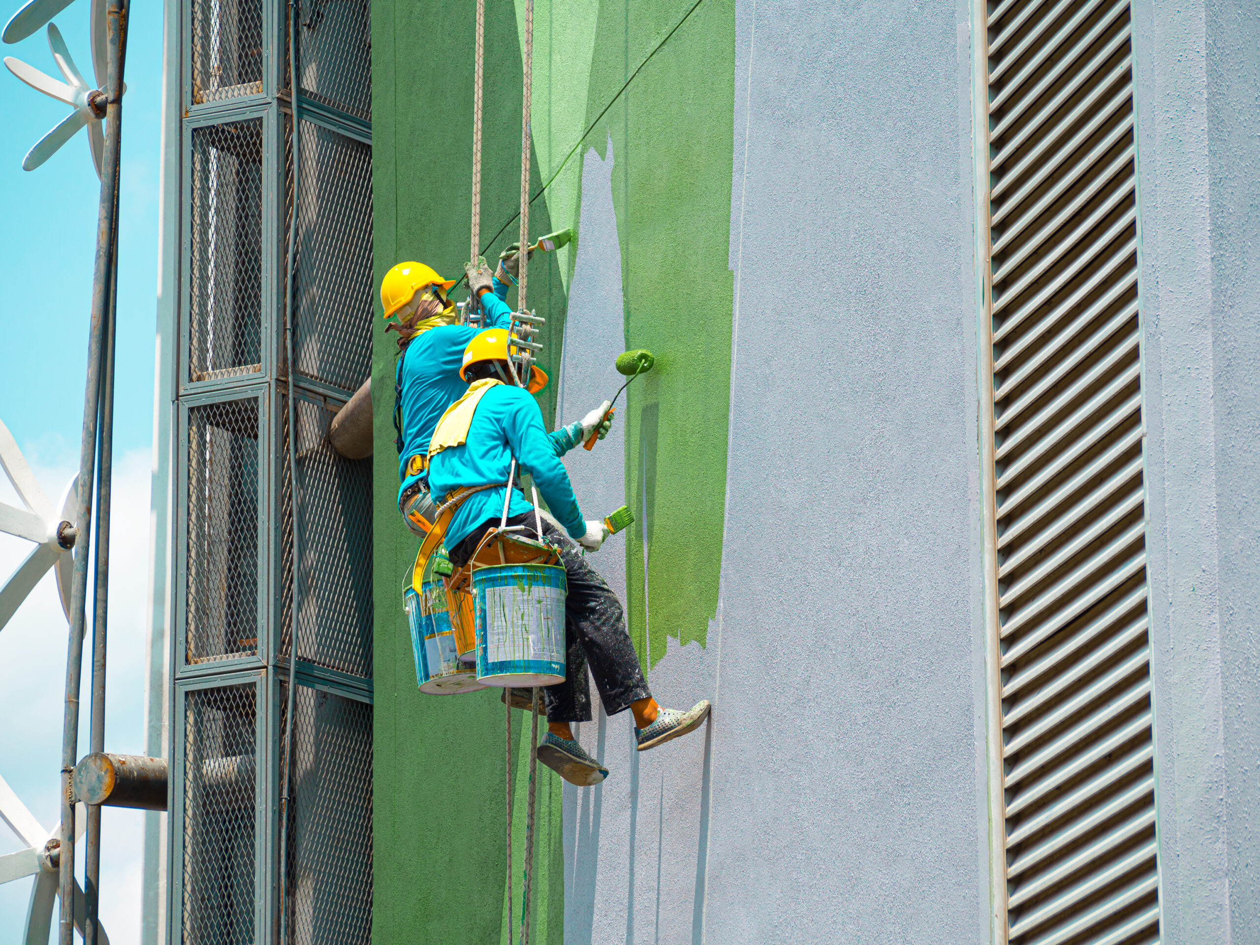 Two painters are painting the exterior of the building on a dangerous looking scaffolding hanging from a tall building with copy space.