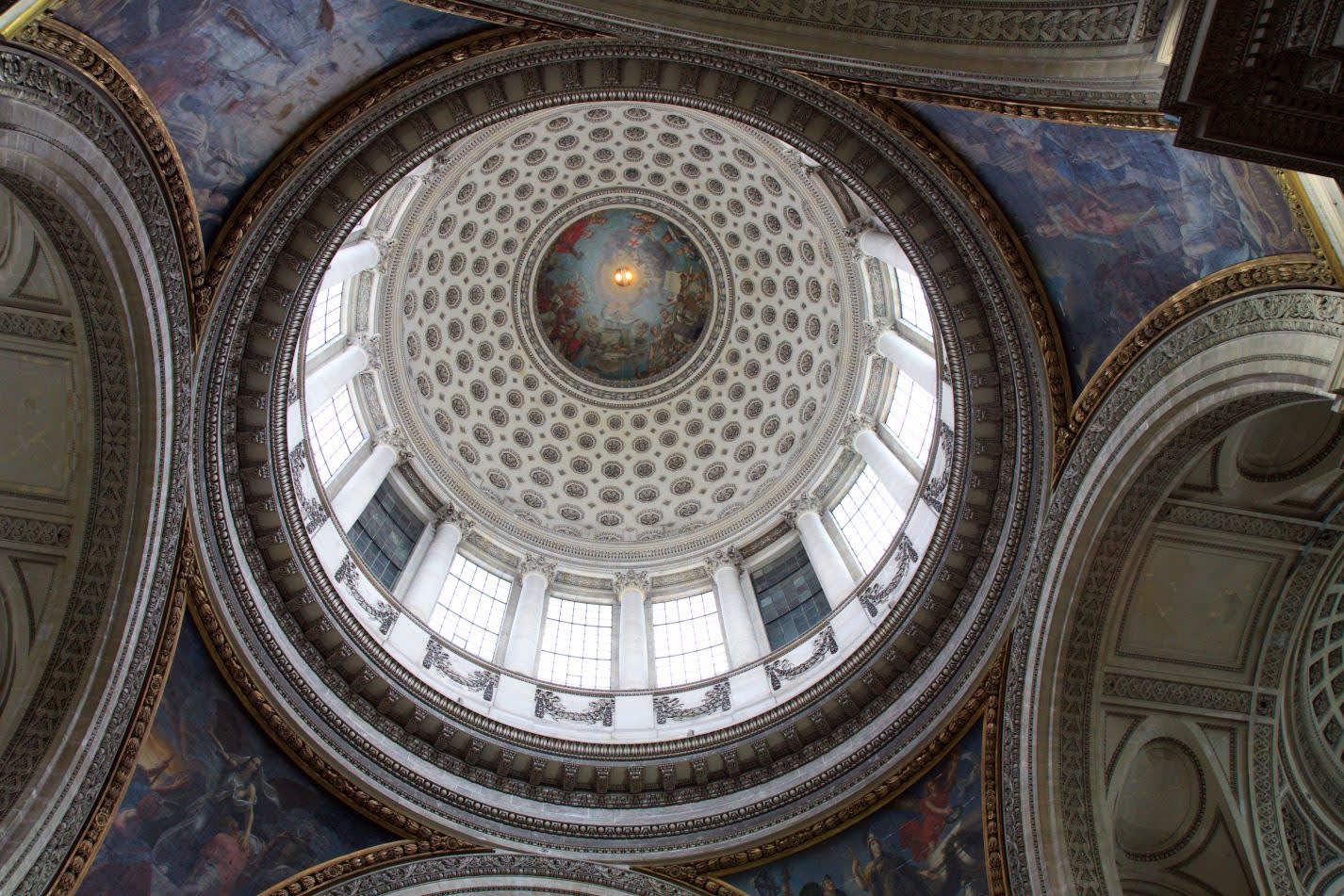 Ornate dome ceiling viewed from below, featuring concentric decorative rings, tall windows, and a central fresco